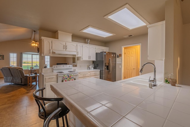 kitchen featuring white range with electric cooktop, tile counters, visible vents, a sink, and stainless steel fridge