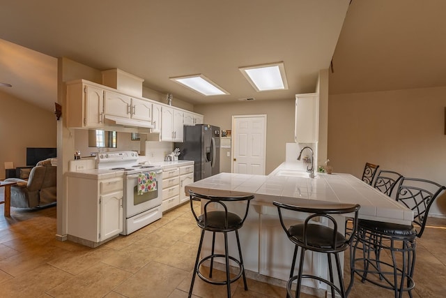 kitchen with a breakfast bar, electric range, a sink, stainless steel fridge, and a peninsula