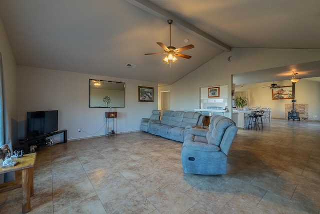 living room featuring ceiling fan, a wood stove, beamed ceiling, and visible vents