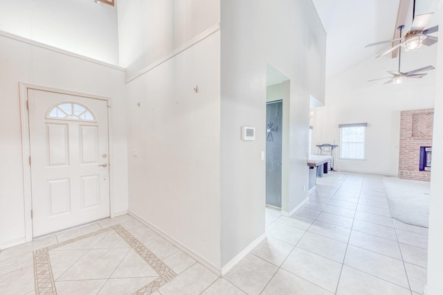 entryway featuring light tile patterned floors, a brick fireplace, ceiling fan, and a high ceiling