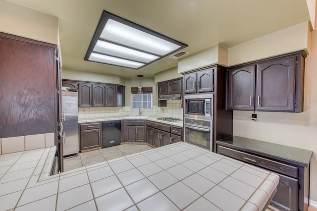 kitchen featuring sink, decorative backsplash, appliances with stainless steel finishes, tile counters, and dark brown cabinetry