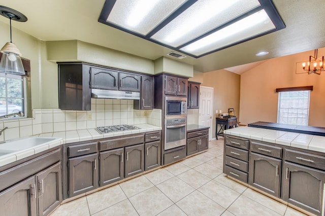 kitchen with tile counters, dark brown cabinetry, appliances with stainless steel finishes, and tasteful backsplash