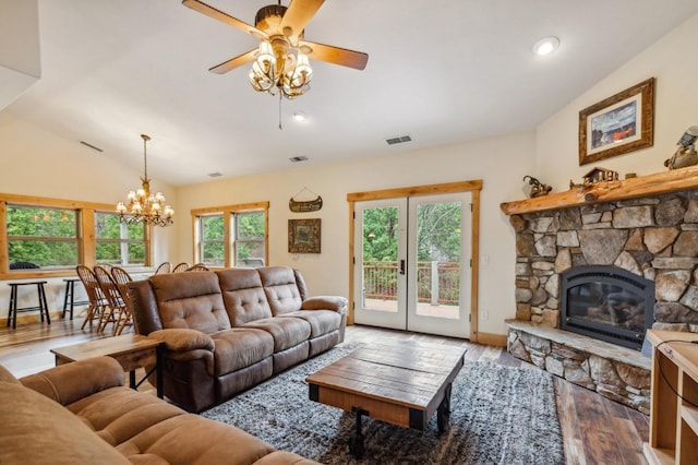 living room featuring a stone fireplace, plenty of natural light, wood-type flooring, vaulted ceiling, and ceiling fan with notable chandelier