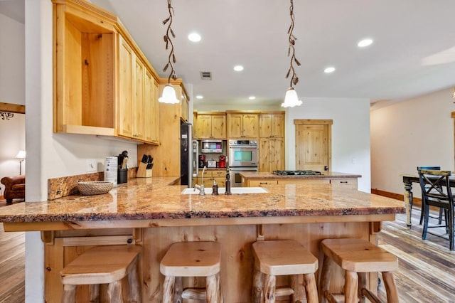 kitchen featuring kitchen peninsula, light brown cabinetry, light hardwood / wood-style floors, and appliances with stainless steel finishes