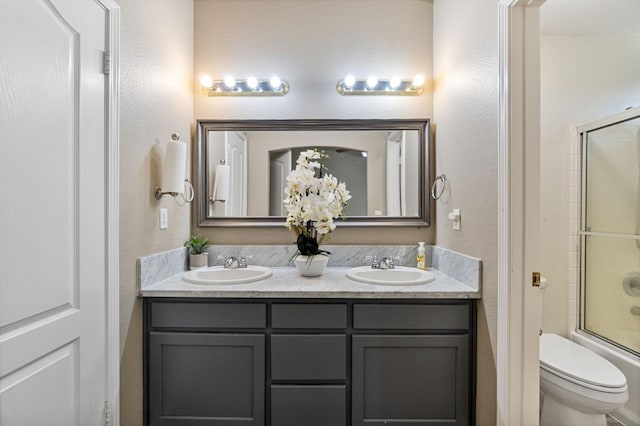 full bathroom featuring double vanity, combined bath / shower with glass door, a sink, and toilet