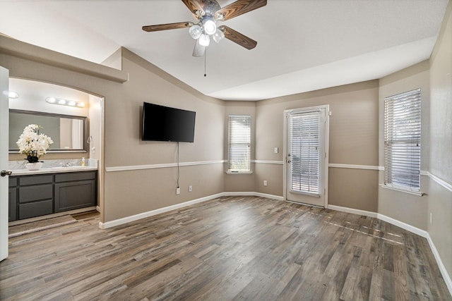 unfurnished living room with a ceiling fan, baseboards, vaulted ceiling, and wood finished floors