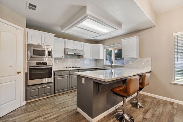 kitchen with stainless steel appliances, gray cabinets, visible vents, under cabinet range hood, and a kitchen bar