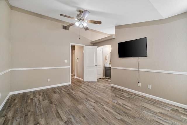 unfurnished bedroom with baseboards, arched walkways, visible vents, wood finished floors, and vaulted ceiling