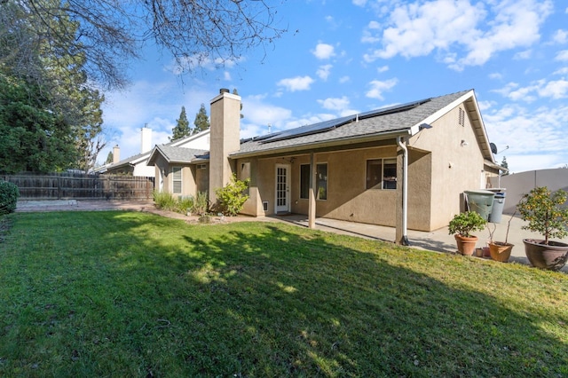 rear view of property with roof mounted solar panels, a patio area, a lawn, and a fenced backyard