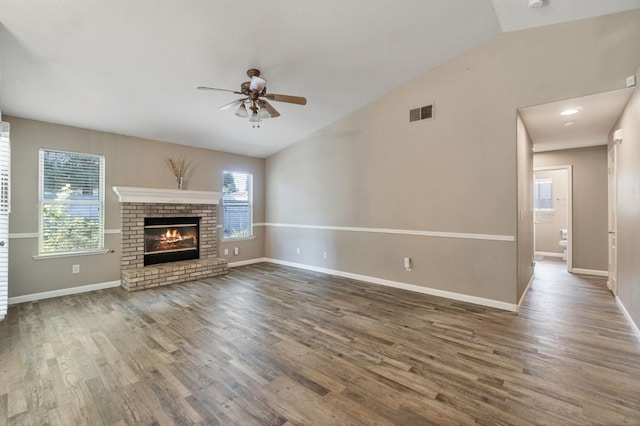 unfurnished living room with vaulted ceiling, ceiling fan, a brick fireplace, and wood finished floors