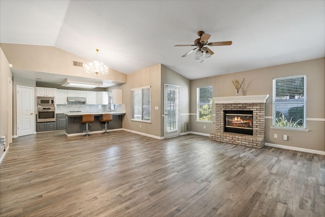 unfurnished living room with visible vents, lofted ceiling, wood finished floors, a fireplace, and ceiling fan with notable chandelier