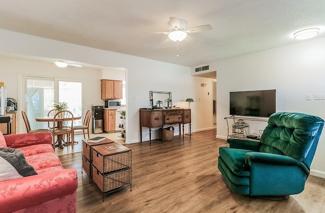 living room with ceiling fan, wood-type flooring, and a textured ceiling