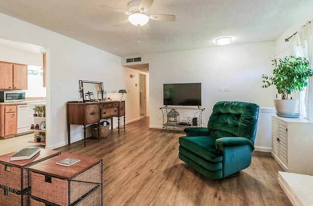 living room with a textured ceiling, light hardwood / wood-style floors, and ceiling fan