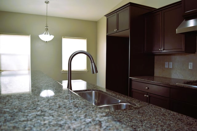 kitchen featuring sink, backsplash, decorative light fixtures, stone countertops, and dark brown cabinets