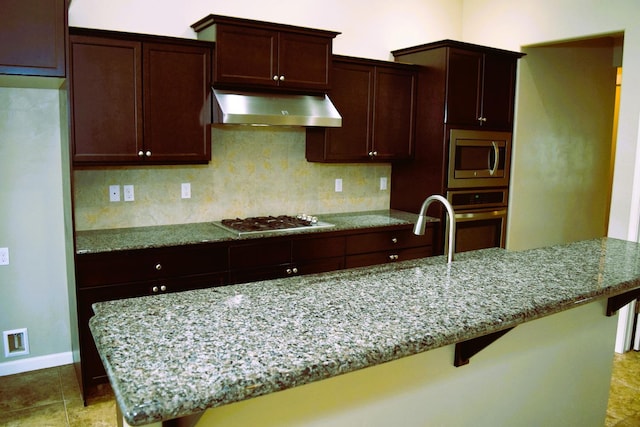 kitchen with a breakfast bar, light stone counters, wall chimney range hood, and appliances with stainless steel finishes