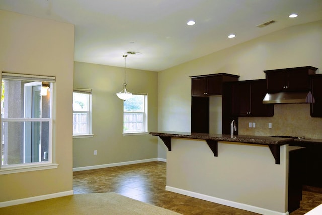 kitchen with dark tile patterned flooring, decorative light fixtures, decorative backsplash, and a breakfast bar area