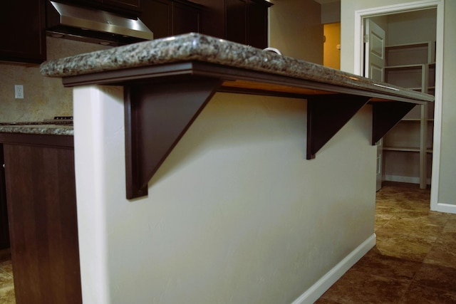 room details featuring a kitchen bar, decorative backsplash, dark brown cabinetry, and stone counters