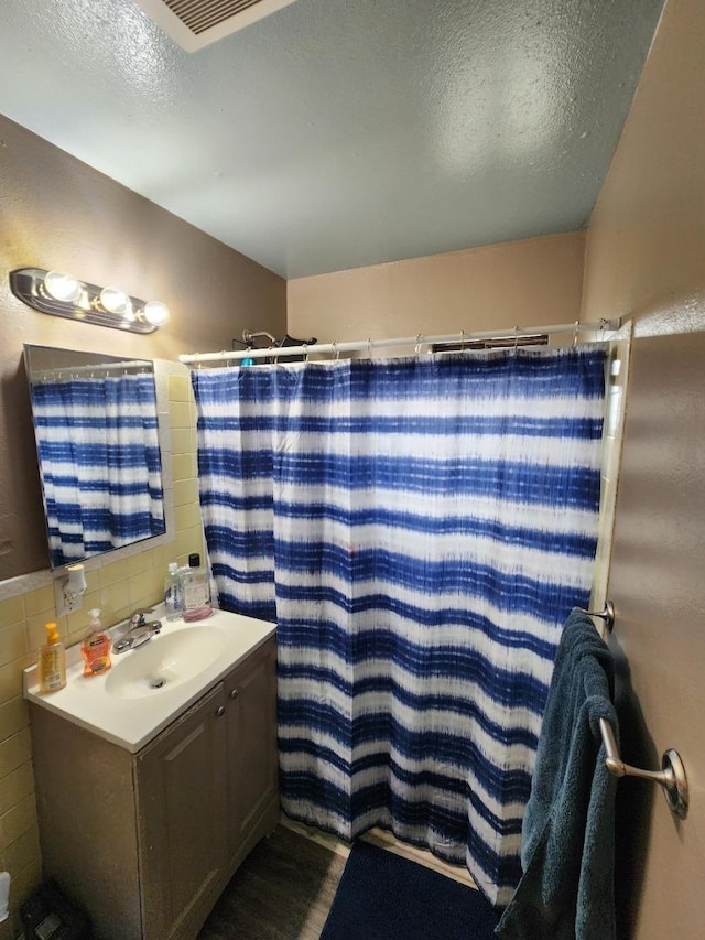 bathroom with a shower with curtain, vanity, a textured ceiling, and tile walls