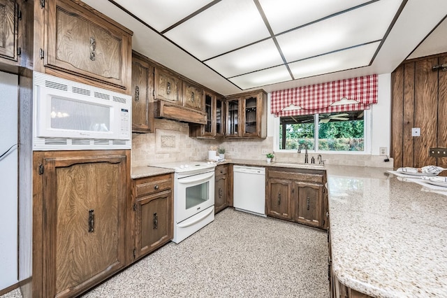 kitchen with light stone countertops, backsplash, custom exhaust hood, white appliances, and sink