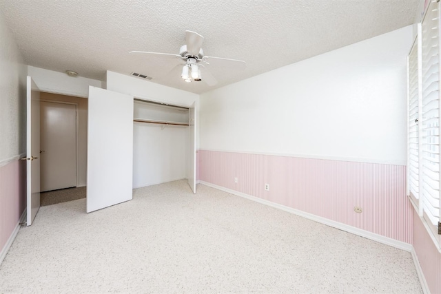 unfurnished bedroom with a textured ceiling, a closet, ceiling fan, and wood walls