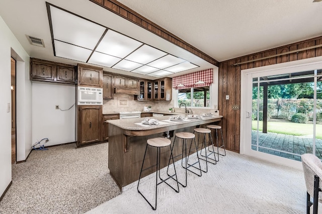 kitchen featuring sink, kitchen peninsula, a kitchen bar, wooden walls, and white microwave