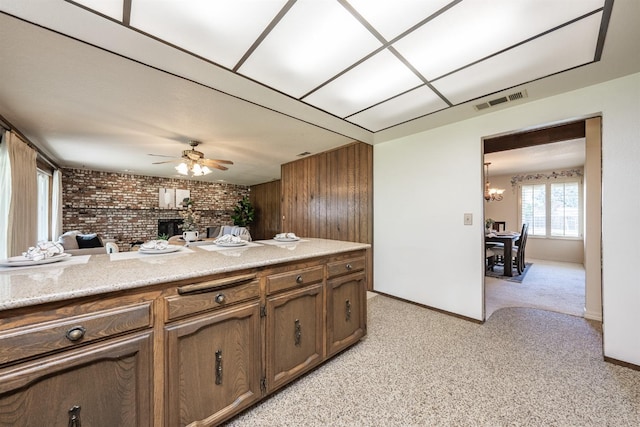 kitchen with a brick fireplace, brick wall, wood walls, light colored carpet, and ceiling fan with notable chandelier