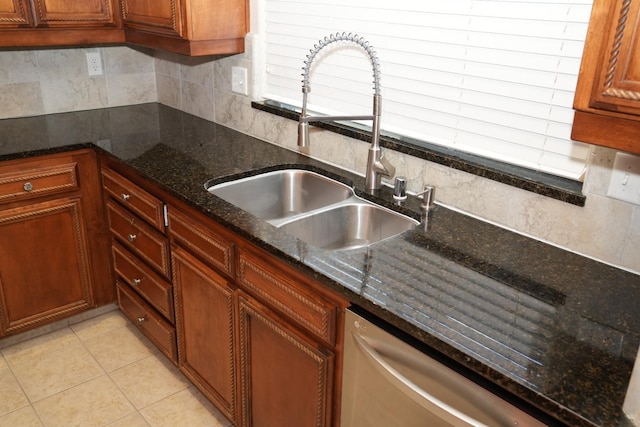 kitchen with backsplash, dark stone counters, sink, stainless steel dishwasher, and light tile patterned floors