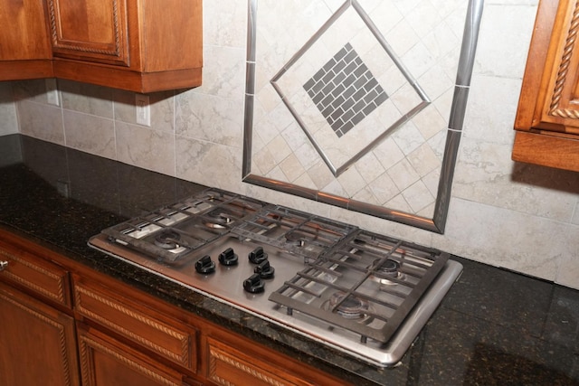 kitchen with tasteful backsplash, stainless steel gas stovetop, and dark stone countertops