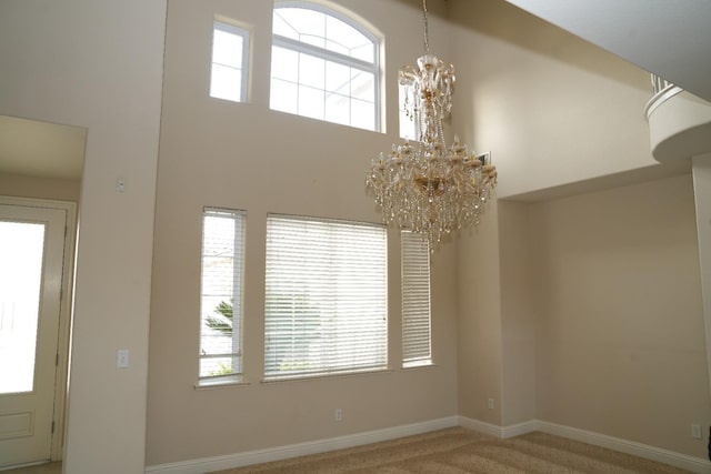 spare room featuring a notable chandelier, carpet floors, and a towering ceiling