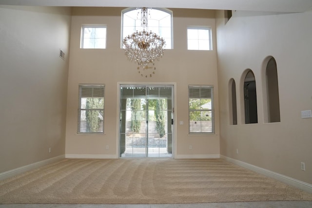 interior space with carpet, plenty of natural light, a towering ceiling, and an inviting chandelier