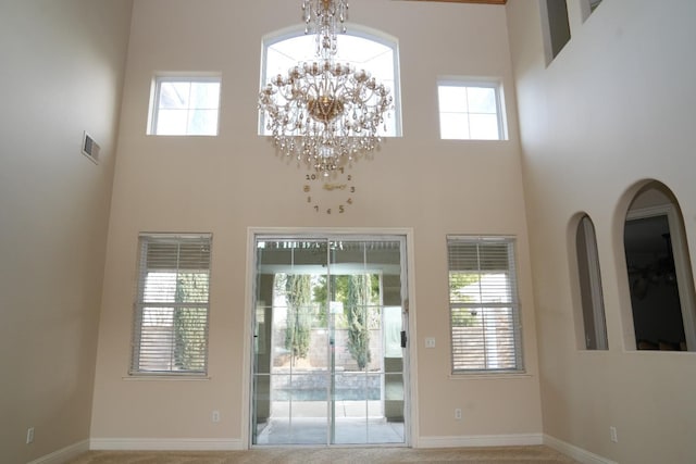 entryway featuring a notable chandelier, a towering ceiling, and carpet floors