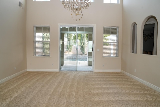 carpeted spare room featuring a high ceiling, an inviting chandelier, and a wealth of natural light