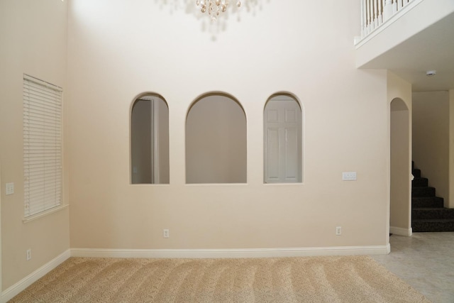 unfurnished room with a notable chandelier, a towering ceiling, and light carpet