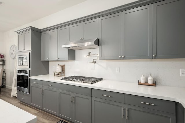 kitchen with stainless steel appliances, gray cabinets, tasteful backsplash, and dark wood-type flooring