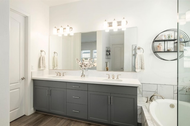 bathroom with hardwood / wood-style floors, a relaxing tiled tub, and vanity