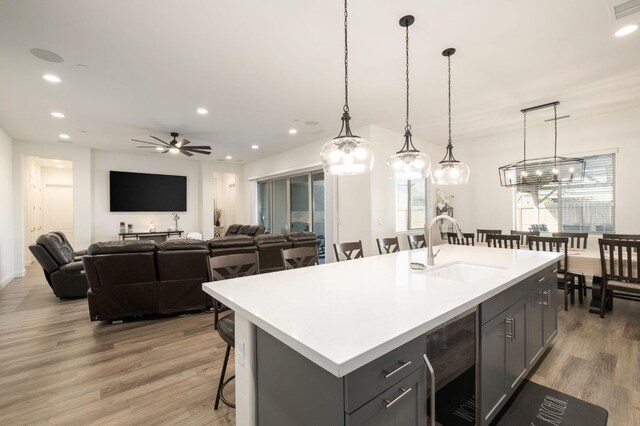 kitchen with ceiling fan, sink, hanging light fixtures, wine cooler, and a center island with sink