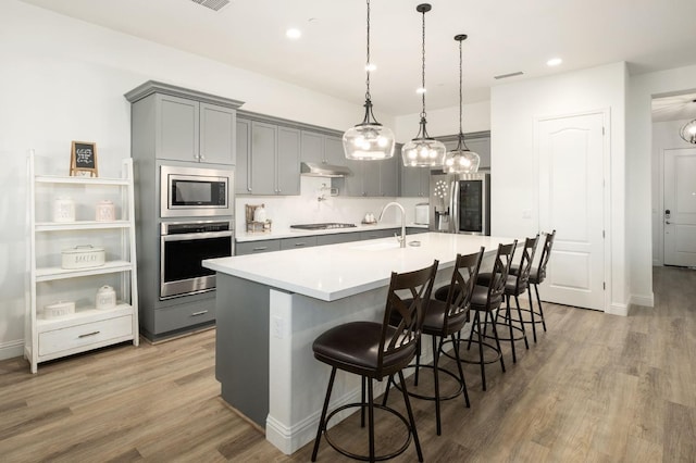 kitchen with a kitchen breakfast bar, stainless steel appliances, sink, decorative light fixtures, and hardwood / wood-style flooring