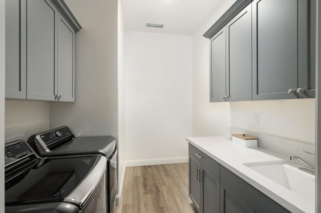 laundry room featuring sink, light hardwood / wood-style flooring, cabinets, and independent washer and dryer