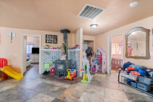 game room with a wood stove and a textured ceiling