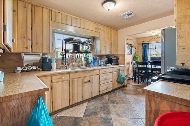 kitchen with appliances with stainless steel finishes, a textured ceiling, light brown cabinetry, and sink