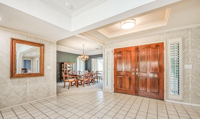 tiled foyer featuring ornamental molding, a raised ceiling, and an inviting chandelier