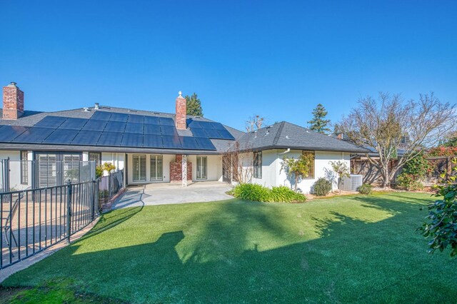 rear view of house with a lawn, solar panels, and a patio