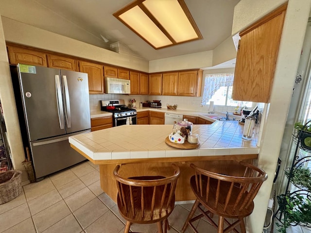 kitchen with kitchen peninsula, tile countertops, stainless steel appliances, and a breakfast bar