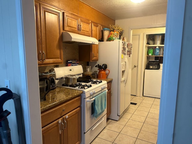 kitchen with washer / dryer, dark stone countertops, a textured ceiling, white appliances, and light tile patterned floors