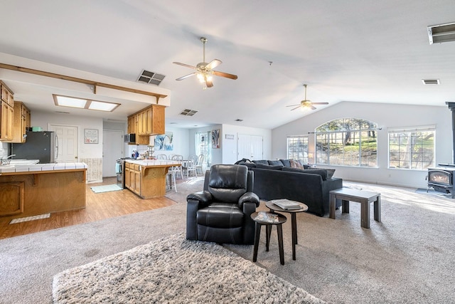 carpeted living room featuring ceiling fan, a wood stove, and vaulted ceiling