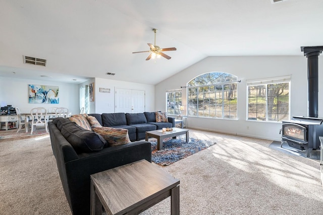 carpeted living room with ceiling fan, a wood stove, and lofted ceiling