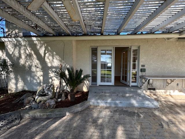 property entrance featuring a pergola, a patio area, and stucco siding