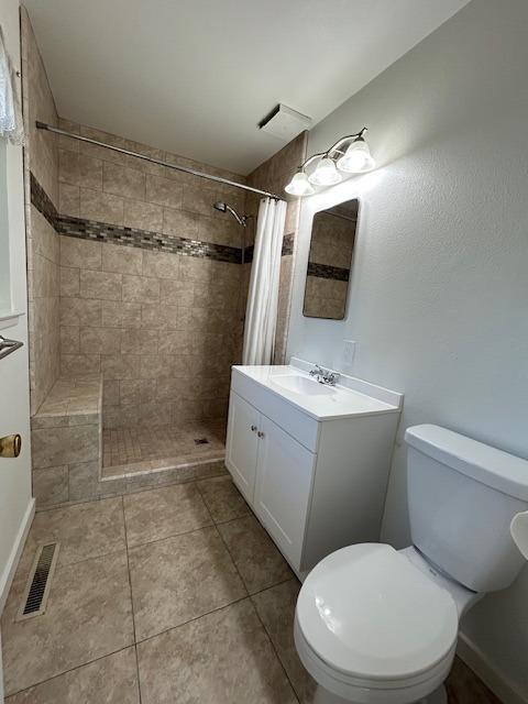 bathroom with tile patterned flooring, vanity, toilet, and walk in shower