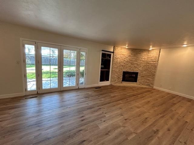 unfurnished living room with a fireplace, wood finished floors, visible vents, baseboards, and french doors