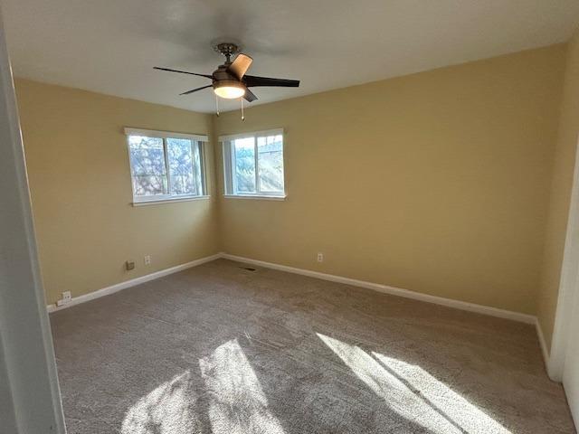 carpeted empty room with ceiling fan and baseboards